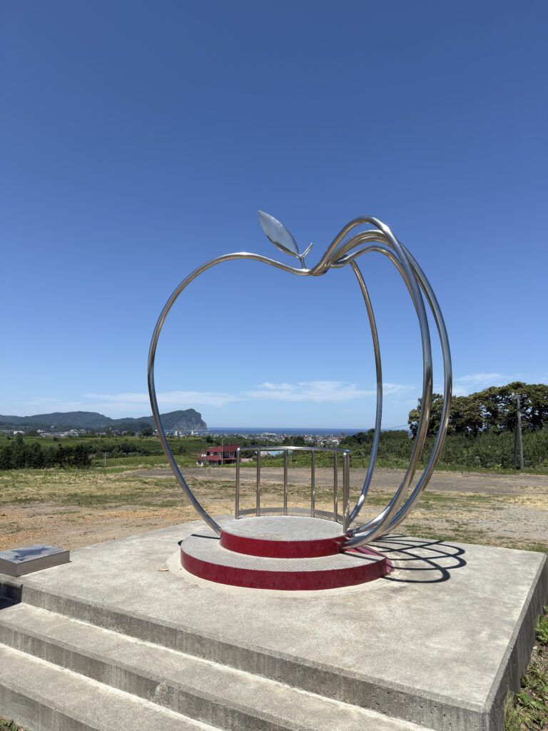 Apple-shaped metal monument overlooking scenic ocean and orchard views in Yoichi, Hokkaido. Popular photo spot in a local fruit farm with panoramic landscapes of the coastline and countryside.