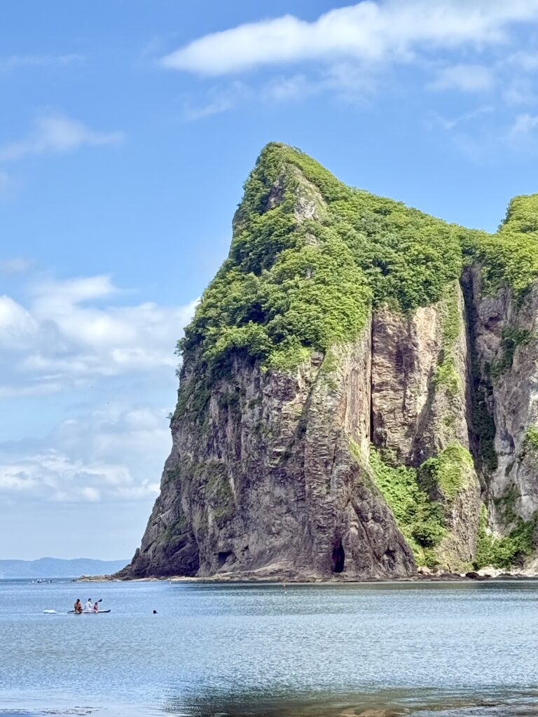Family enjoying tidepooling and stand-up paddleboarding in the clear waters of Yoichi, Hokkaido, with scenic Ebisu Rock in the background – a hidden gem for nature lovers