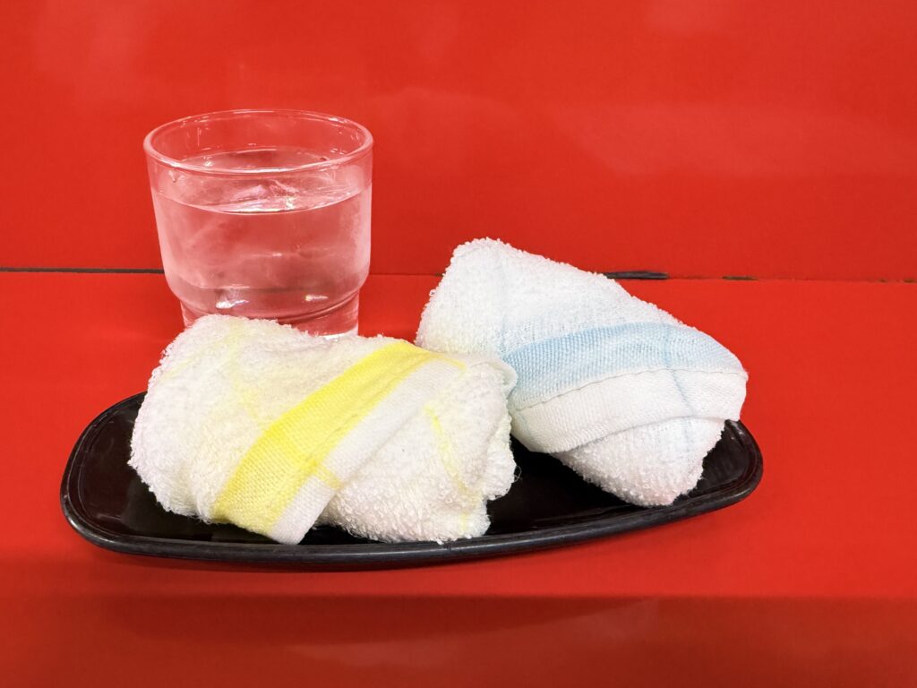 ラーメン店なかまの赤いテーブルに置かれた水とおしぼり