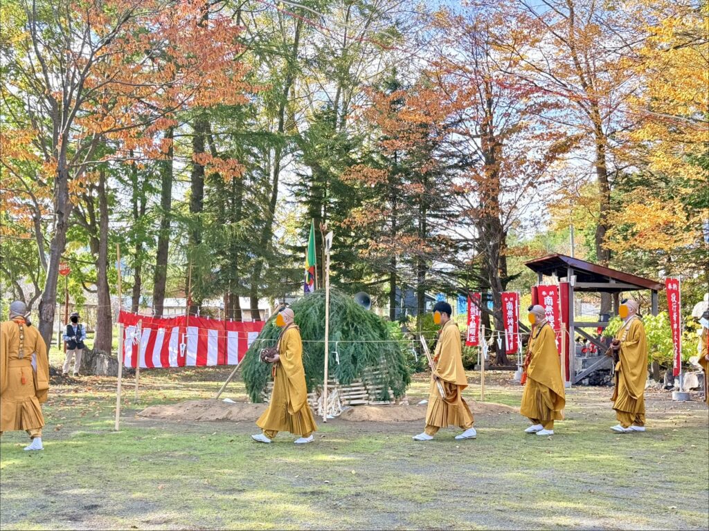 倶知安町の金毘羅寺秋季例大祭で、火渡り前の木組みの周囲を歩く僧侶たちと秋の紅葉
