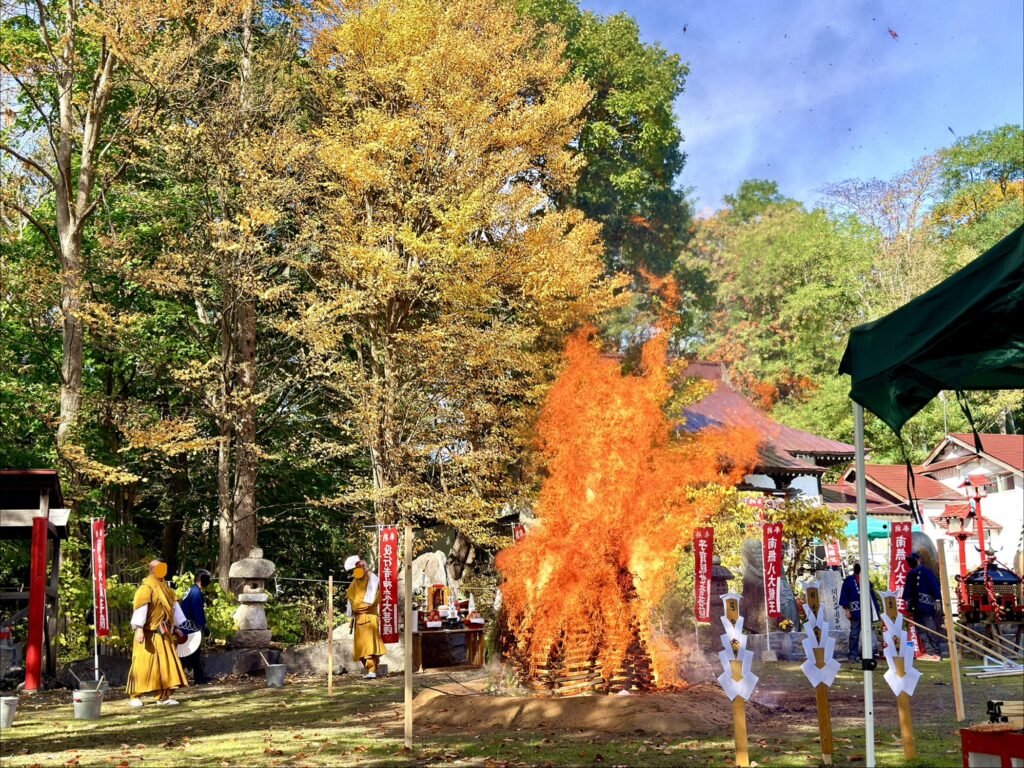 倶知安・金毘羅寺の火渡りの儀で紅葉を背景に大きく燃え上がる炎