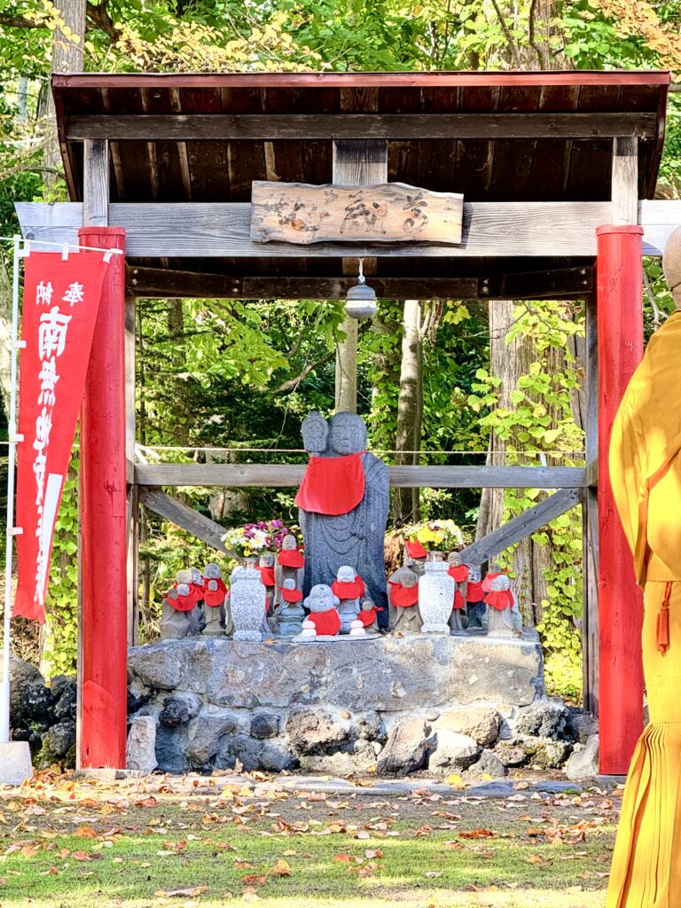 倶知安町の金毘羅寺境内にある木造の祠と赤い前掛けを着けたお地蔵さまたち