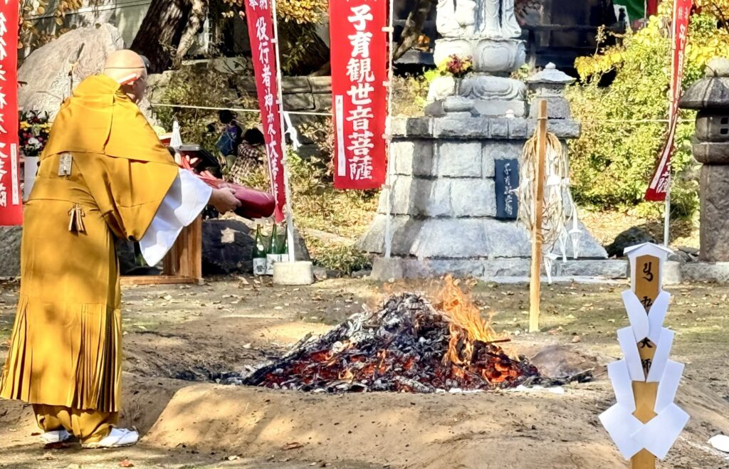 倶知安・金毘羅寺の火渡りで僧侶が赤い持ち物を残り火にかざす様子