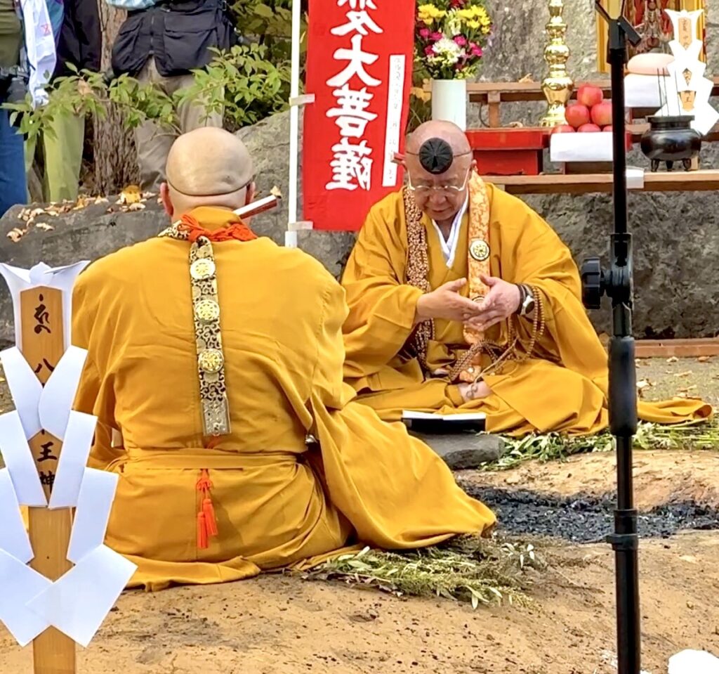 倶知安町の金毘羅寺の火渡りで炭を前に座り数珠を手にする黄色い法衣の僧侶たち