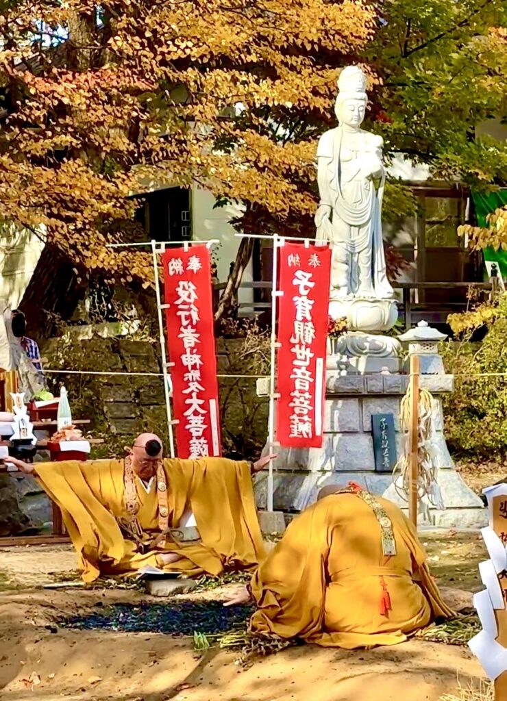 倶知安町の金毘羅寺で火渡りの炭を前に両腕を広げて儀式を行う僧侶と秋の紅葉